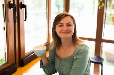 Güzel bir kadın kahve içiyor ve bir kafede kameraya bakıyor. Bir kadın en sevdiği kahveyi içer, bu da ona zevk verir..