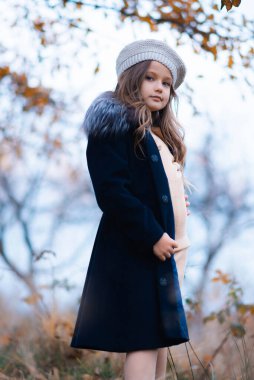 A girl in a dark blue coat outside has a sad look looking at the camera. Autumn portrait