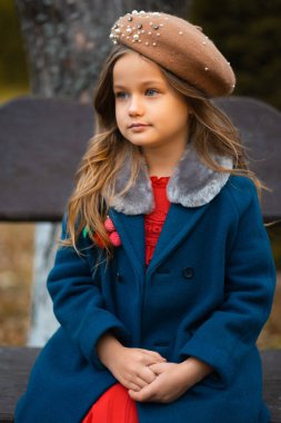 Sad child sitting on a park bench in old fashion clothes. Fashion portrait