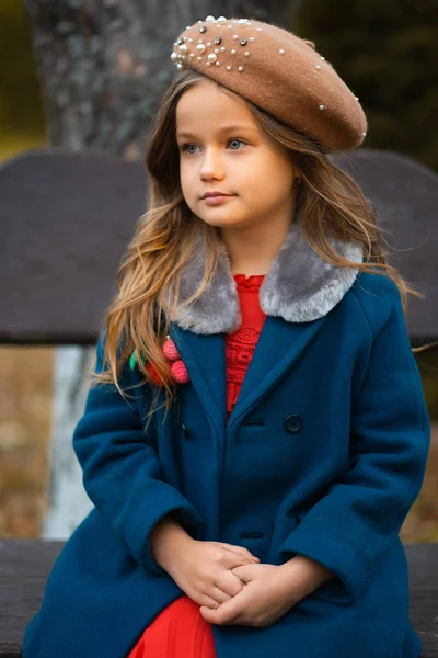 Sad child sitting on a park bench in old fashion clothes. Fashion portrait