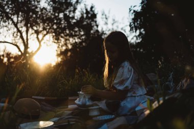Pikniğe giden bir kız gün batımında kendine çay doldurur.