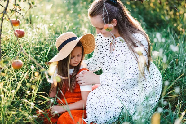 Anne ve kızı sonbahar elma bahçesinde. Anne kızını okşuyor.