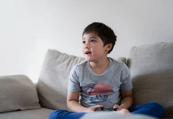 若い男の子がオンラインでビデオゲームをプレイし キャンディショットソファ保持ゲームコンソールに座って幸せなかわいい子供を撮影しました 週末に家でリラックスしている間に肖像画の子供の顔 — ストック写真