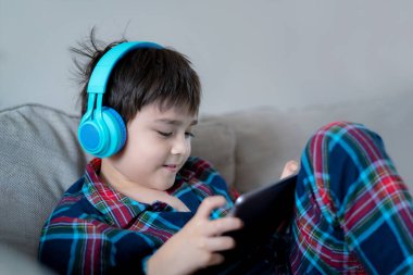 Kulaklık takan, müzik dinleyen mutlu çocuk, gülen yüzlü çocuk tatilde arkadaşlarıyla tablette oyun oynarken çocuk, sabahları evde dinlenirken Noel pijamaları giyen çocuk.