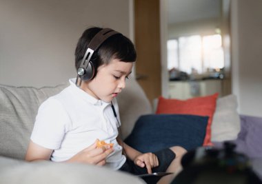 Kulaklık takan, müzik dinleyen, internet, e-öğrenme, sosyal ağ konsepti olan çocuklar hakkında dijital tablet arayarak ödev yapan çocuk.