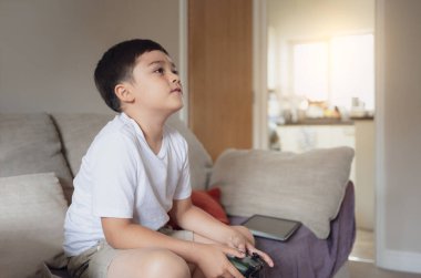 Video oyunu kontrolü elinde tutan mutlu bir çocuğun portresi. Evde online oyun oynayan bir çocuk, kanepede oturan genç bir çocuk oyuncakla eğleniyor ve hafta sonları dinleniyor.