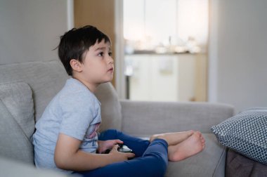 Mutlu genç çocuk arkadaşlarıyla online video oyunları oynuyor, Samimi çocuk kanepede oturmuş oyun konsolu tutuyor. Portre çocuğu oyun oynarken ve evde dinlenirken monitöre ya da televizyona bakıyor.