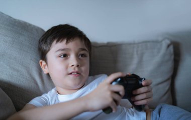 Mutlu genç çocuk arkadaşlarıyla online video oyunları oynuyor, Samimi çocuk kanepede oturmuş oyun konsolu tutuyor. Portre çocuğu oyun oynarken ve evde dinlenirken monitöre ya da televizyona bakıyor.