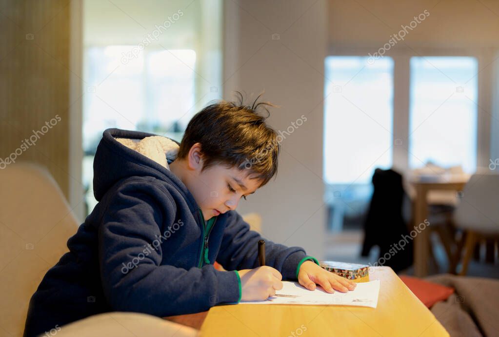 School kid using black pen drawing or writing the letter on paper, Young boy doing homework, Child with pen writing notes in paper sheet during the lesson.Cute pupil doing test, Homeschooling concept