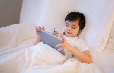 Mutlu Çocuk elinde tabletle yatıp çizgi film seyrediyor ve dijital ekranda arkadaşlarıyla sohbet ediyor. İnternette oyun oynayan tatlı bir çocuk. Okula gitmeden önce çocuk dinleniyor.