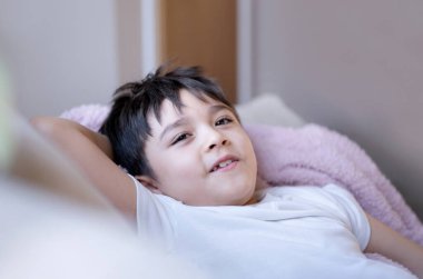 Portre mutlu yong çocuk kanepede uzanıyor, evde dinleniyor, kameraya gülümseyen yüzüyle bakan sevimli çocuk, haftasonu kanepede oturan pozitif çocuk eğleniyor.