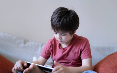Okul çocuğu kanepede oturmuş tablette çizgi film seyrediyor, şirin çocuk dijital ekranda oyun oynuyor, kapalı mekan portresi çekiyor, ders odasında tek başına eğleniyor ve dinleniyor.