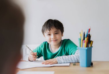 Mutlu çocuk kalem çiziyor ya da kağıda resim çiziyor, gülümseyen yüzü olan sevimli çocuk masaya oturuyor, ödevlerini yapıyor, çocuk arkadaşlarıyla sanat ve zanaat faaliyetlerini, eğitim kavramını seviyor.