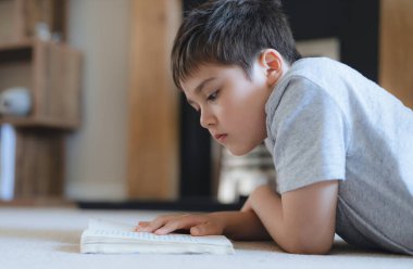 Ev ödevi için kitap okuyan portre okulu çocuğu, halıya uzanmış çocuk oturma odasında hikaye okumaktan, hafta sonları evde dinlenmekten zevk alıyor. Ev Okulu ya da Eğitim Konsepti
