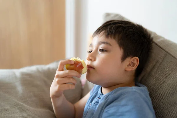 健康的な子供は赤いリンゴを食べ かわいい男の子はリビングルームでテレビを見ながら彼のスナックのために新鮮な果物を食べて 子供の顔を閉じて食べ物を食べています 子供のための健康食品コンセプト — ストック写真