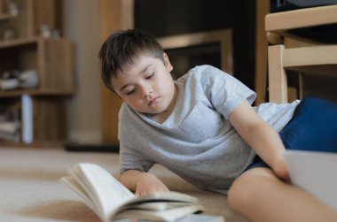 Ev ödevi için kitap okuyan portre okulu çocuğu, halıya uzanmış çocuk oturma odasında hikaye okumaktan, hafta sonları evde dinlenmekten zevk alıyor. Ev Okulu ya da Eğitim Konsepti