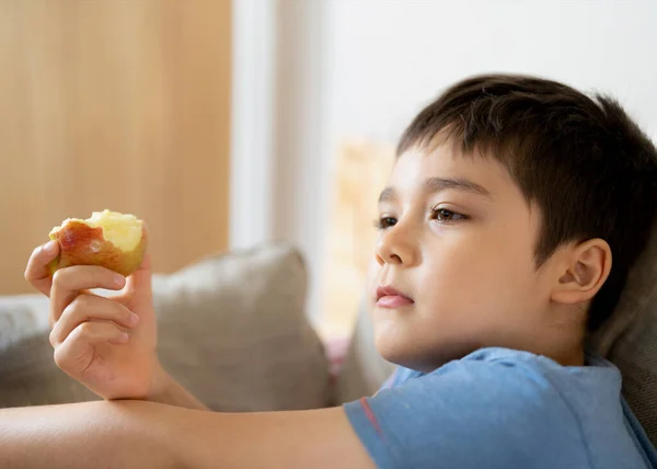 健康的な子供は赤いリンゴを食べ かわいい男の子はリビングルームでテレビを見ながら彼のスナックのために新鮮な果物を食べて 子供の顔を閉じて食べ物を食べています 子供のための健康食品コンセプト — ストック写真