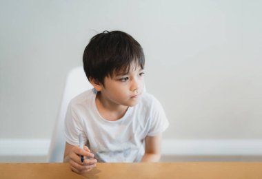 Siyah kalemle derin düşüncelere dalmış portre tutan genç, düşünen yüzüyle dışarı bakan okul çocuğu. Meraklı yüzlü çocuk masada yalnız oturuyor.