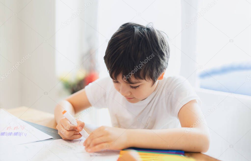 School kid using colour pen drawing or writing the letter on paper, Young boy doing homework, Child with pen writing notes in paper sheet during the lesson.Cute pupil doing test, Homeschooling concept