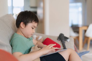 İnternette tablet oyunu oynayan küçük bir çocuk kanepede oturan ya da arkadaşıyla internetten konuşan bir çocuk, sabah oturma odasında dinlenen çocuk, yeni teknoloji konsepti olan çocuklar.