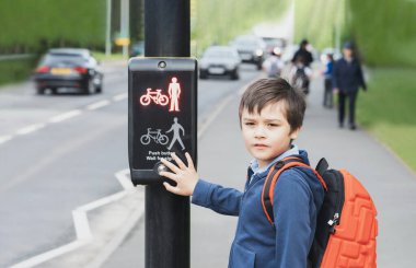 Okul çocuğu okula giderken yaya geçidinde trafik ışıklarında düğmeye basıyor. Trafik ışığı kullanan sırt çantalı çocuk karşıya geçmek için yaya tesislerini kontrol ediyordu..