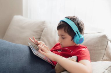 İnternette arkadaşlarıyla oyun oynamak için kulaklık takan mutlu genç çocuk, kanepede oturup kitap okuyan ya da tablette çizgi film izleyen çocuk, evde ödev yapan okul çocuğu..