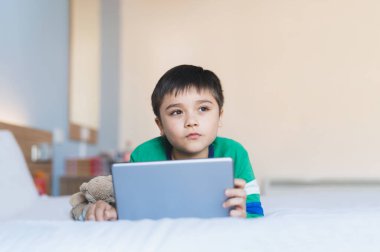 Portre Çocuk internette internette oyun oynuyor, küçük çocuk tablet kullanıyor, sabahları arkadaşlarıyla yazışıyor, sohbet ediyor, hafta sonları yatakta dinleniyor..