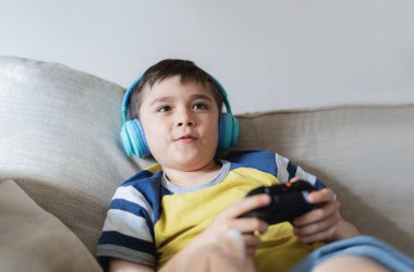 Kulaklık takan ve video oyunu oynayan portre çocuğu. Çocuk evde arkadaşlarıyla konsol oyunu oynuyor, genç çocuk kanepede oturuyor ve hafta sonları tek başına eğleniyor.