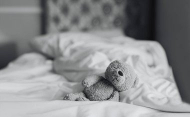 Oyuncak ayı yatak odasında uzanıyor. Pencereden güneş ışığı parlıyor. Siyah beyaz fotoğraf. Yalnız kahverengi ayı evde yalnız kalıyor.