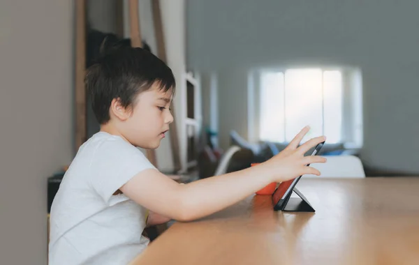 Kid playing game online with friends on tablet, Cinematic portrait young boy video call with friends while having breakfast,Child watching cartoon on internet, School kid doing homework on digital pad