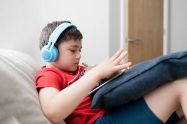 İnternette arkadaşlarıyla oyun oynamak için kulaklık takan mutlu genç çocuk, kanepede oturup kitap okuyan ya da tablette çizgi film izleyen çocuk, evde ödev yapan okul çocuğu..