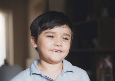 Sinematik Portre Çocuğu derin düşüncelere dalmış gülümseyen yüzüyle dışarı bakan mutlu genç çocuk. Akşam vakti oturma odasında tek başına oynayan bir çocuk..