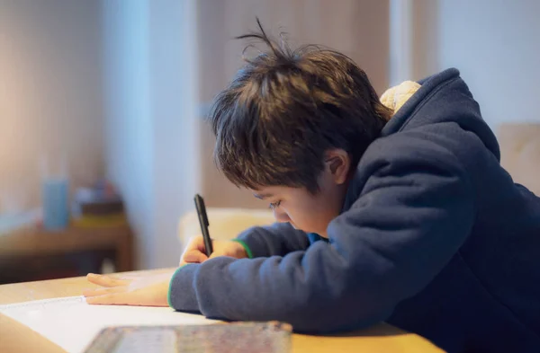 Kid siting on table doing homework,Child boy holding black pen writing on white paper,Young boy practicing English words at home. Elementary school and home schooling, Distance Education concept