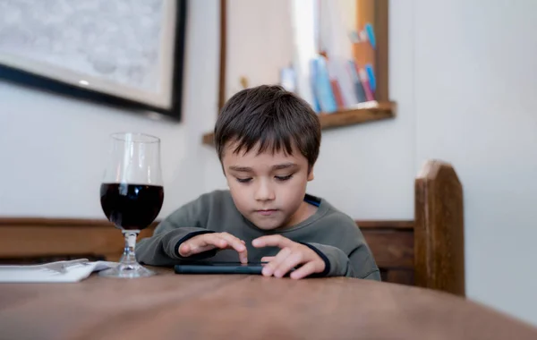 Kid playing game on mobile while waiting for food, Portrait young boy sitting in coffee shop sending text to friends,Child playing game online on cellphone.Children with internet or technology concept