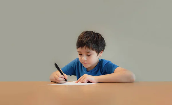 Kid siting on table doing homework,Child boy holding black pen writing on white paper,Young boy practicing English words at home. Elementary school and home schooling, Distance Education concept