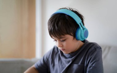 Close up face Happy kid wearing headphones listening to music,  Concentrated boy deep in thought with listening homework. Side view portrait Cute child enjoy creative activity at home on weekend.
