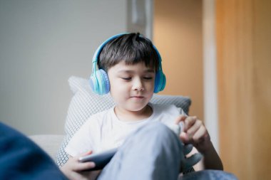 Arkadaşlarıyla internette oyun oynamak için kulaklık takan mutlu genç çocuk, pencere kenarında oturup tablette çizgi film izleyen çocuk, evde ödev yapan okul çocuğu..