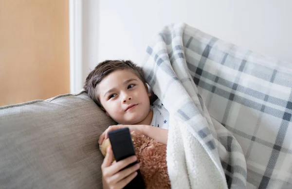 Kid sitting on sofa watching TV, A boy holding remote control and looking up with smiling face, Positive child lying on sofa enjoy watching cartoon on TV, Kid relaxing at home on weekend