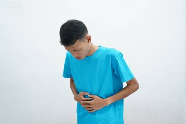 Mavi tişört giyen Asyalı adam mide bulantısı ve acı veren bir hastalıktan dolayı elini karnına koyar. hastalıklı kavram.