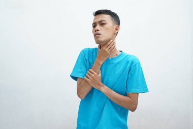 Genç adamın boğazı ağrıyor ve boynuna dokunuyor. Beyaz arka planda mavi tişört giyiyor. Yutması zor.