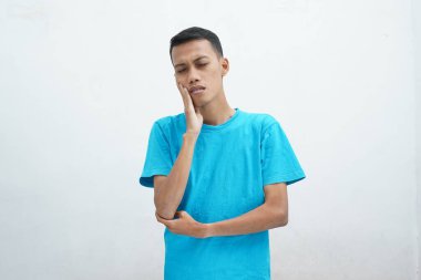 Diş ağrısı konsepti. Mavi tişört giyen genç adam acı çekiyor, şiddetli diş ağrısından muzdarip, acı dolu bir ifadeyle. İzole edilmiş beyaz arkaplan.