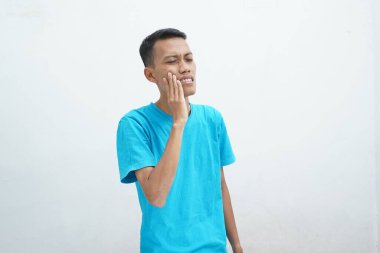 Diş ağrısı konsepti. Mavi tişört giyen genç adam acı çekiyor, şiddetli diş ağrısından muzdarip, acı dolu bir ifadeyle. İzole edilmiş beyaz arkaplan.