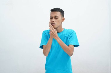 Diş ağrısı konsepti. Mavi tişört giyen genç adam acı çekiyor, şiddetli diş ağrısından muzdarip, acı dolu bir ifadeyle. İzole edilmiş beyaz arkaplan.