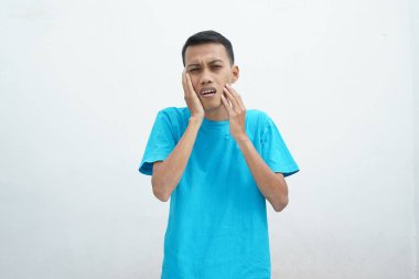 Diş ağrısı konsepti. Mavi tişört giyen genç adam acı çekiyor, şiddetli diş ağrısından muzdarip, acı dolu bir ifadeyle. İzole edilmiş beyaz arkaplan.