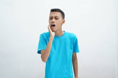 Diş ağrısı konsepti. Mavi tişört giyen genç adam acı çekiyor, şiddetli diş ağrısından muzdarip, acı dolu bir ifadeyle. İzole edilmiş beyaz arkaplan.