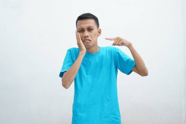 Diş ağrısı konsepti. Mavi tişört giyen genç adam acı çekiyor, şiddetli diş ağrısından muzdarip, acı dolu bir ifadeyle. İzole edilmiş beyaz arkaplan.