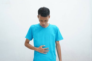 Mavi tişört giyen Asyalı adam mide bulantısı ve acı veren bir hastalıktan dolayı elini karnına koyar. hastalıklı kavram.