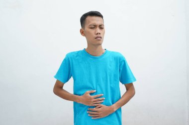 Mavi tişört giyen Asyalı adam mide bulantısı ve acı veren bir hastalıktan dolayı elini karnına koyar. hastalıklı kavram.