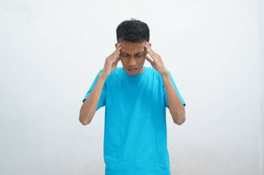Mavi tişört giyen Asyalı genç adamın portresi şiddetli baş ağrısından muzdarip, parmaklarını şakağa bastıran, acıyı dindirmek için gözlerini kapatan çaresiz yüz ifadesiyle.