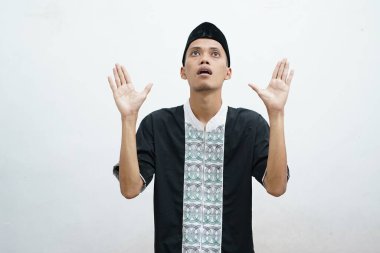 Asyalı Müslüman bir adam ellerini uzatarak onlara yukarıdan ulaşan ve beyaz arka planda izole edilmiş bir şeyden korunuyor.